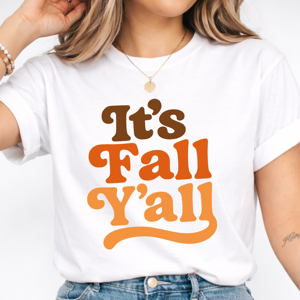 Woman wearing a white It’s Fall Y’all graphic tee with brown and orange retro lettering.