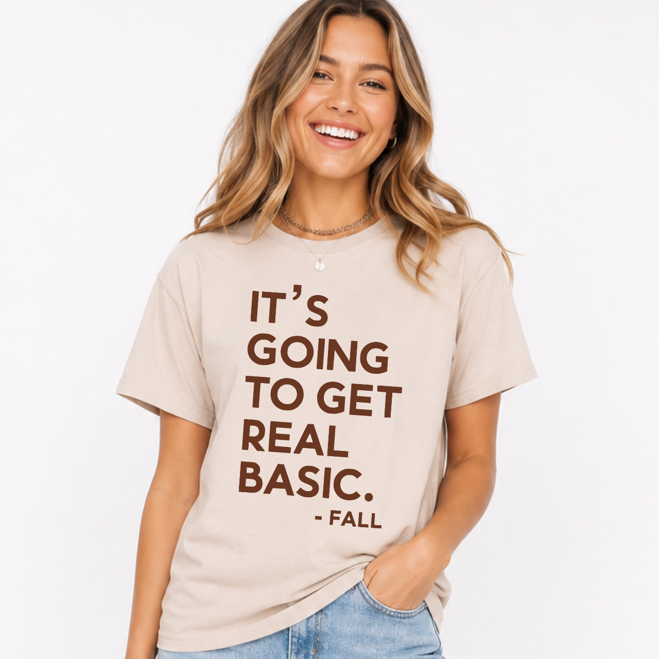Woman wearing a sand It’s Going to Get Real Basic fall graphic tee with bold brown lettering.