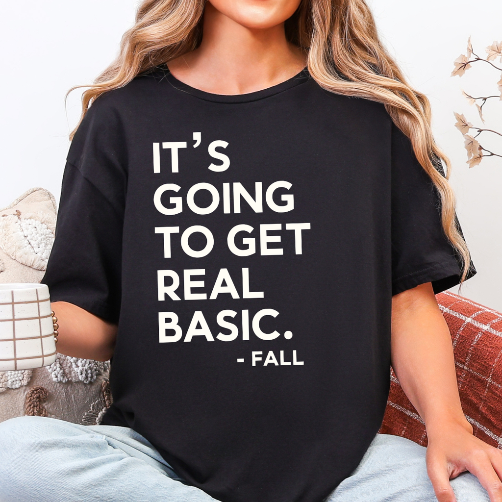 Woman wearing a black It’s Going to Get Real Basic fall graphic tee with bold brown lettering.