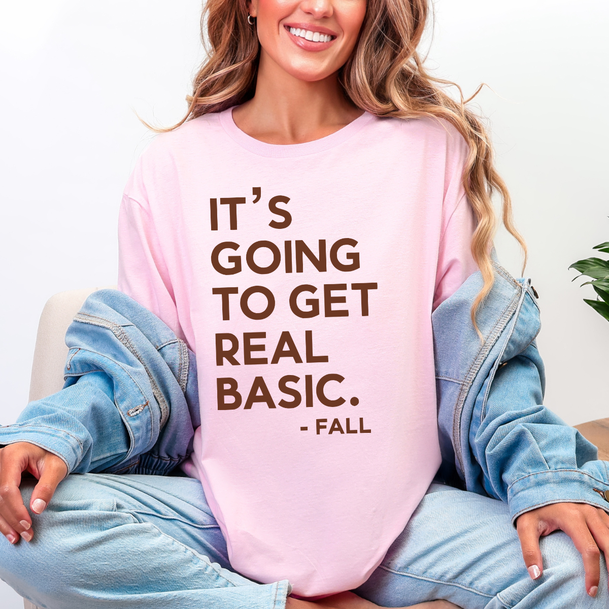 Woman wearing a light pink It’s Going to Get Real Basic fall graphic tee with bold brown lettering.