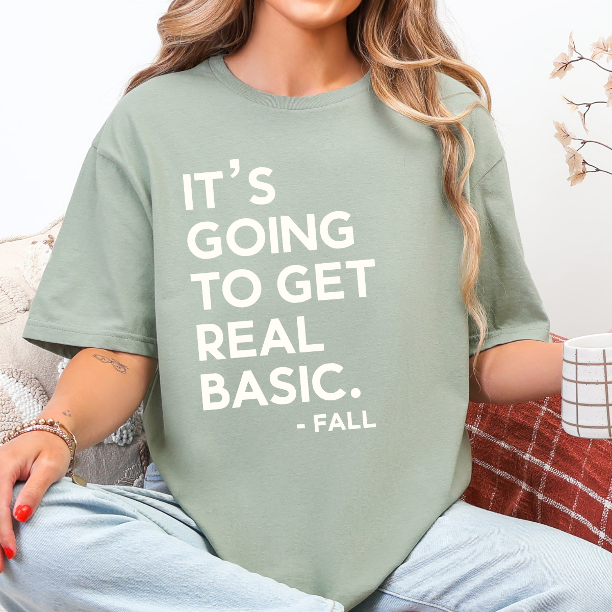 Woman wearing a sage It’s Going to Get Real Basic fall graphic tee with bold brown lettering.