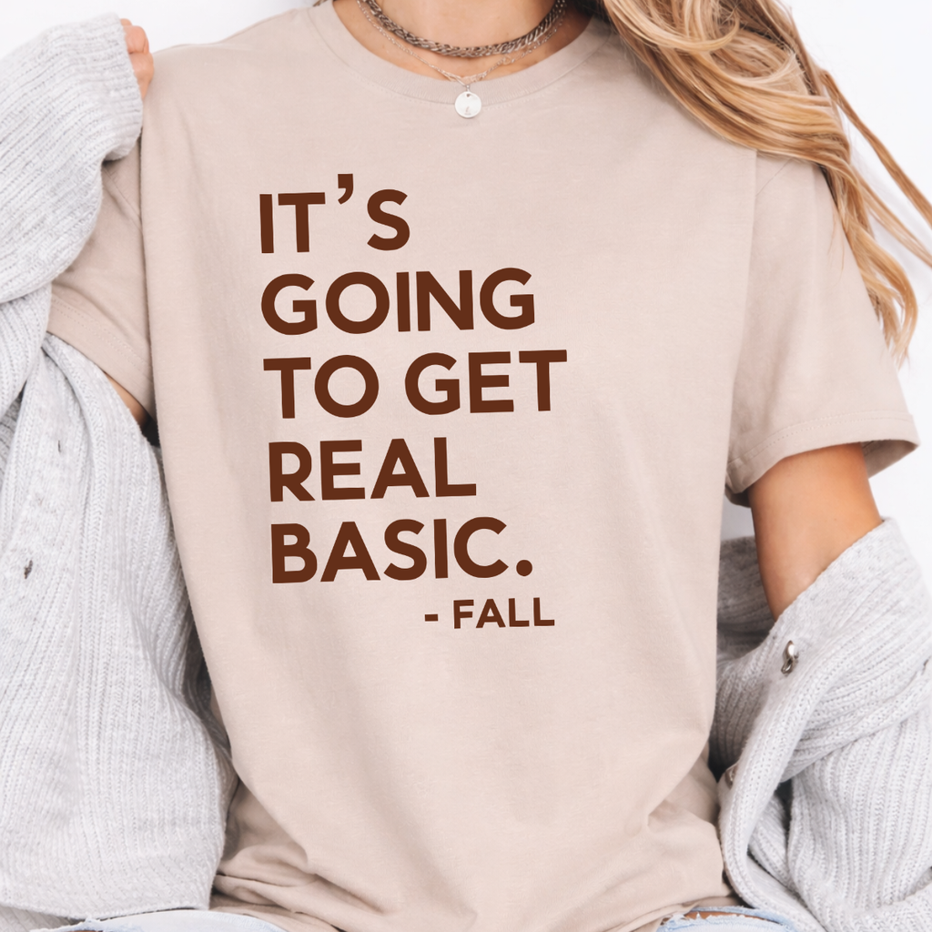 Woman wearing a sand It’s Going to Get Real Basic fall graphic tee with bold brown lettering.
