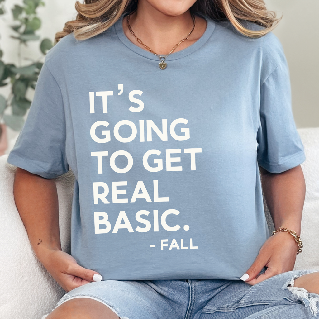 Woman wearing a stone blue It’s Going to Get Real Basic fall graphic tee with bold brown lettering.
