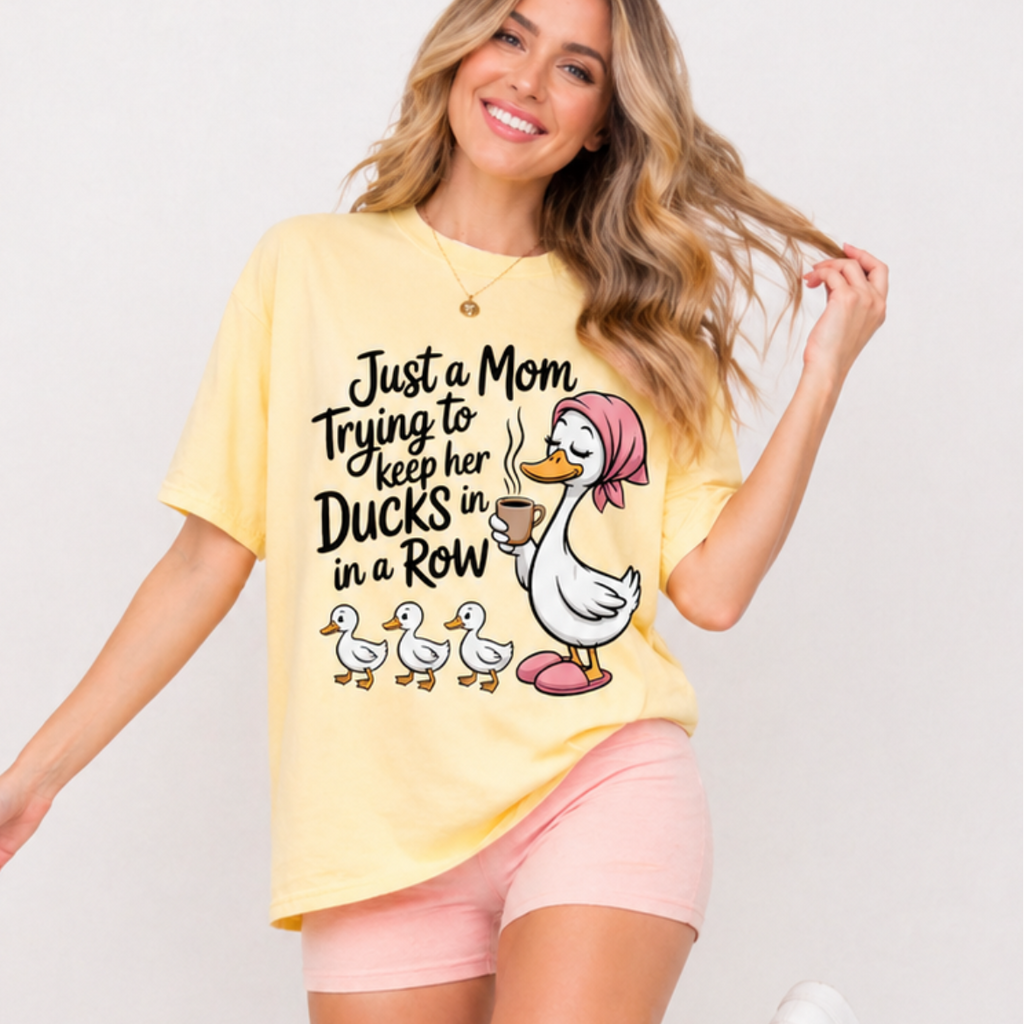 Woman wearing a yellow t-shirt with a graphic and text that says 'Just a Mom Trying to Keep Her Ducks in a Row.'