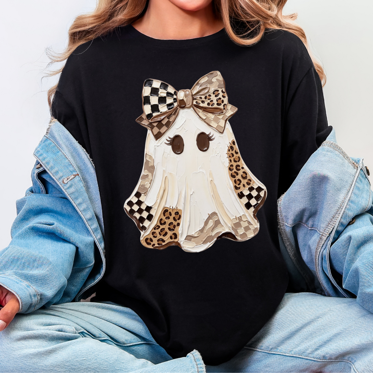 Woman wearing a black Halloween graphic tee with a white ghost, leopard print and checkered details, and a large bow.
