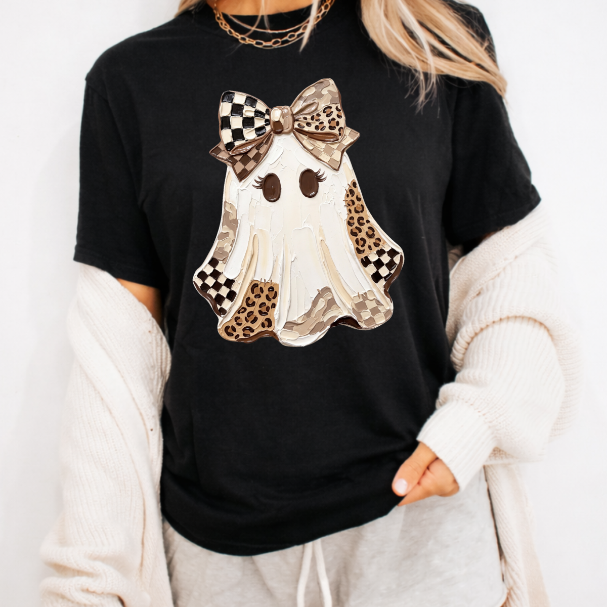 Woman wearing a black Halloween graphic tee with a white ghost, leopard print and checkered details, and a large bow.