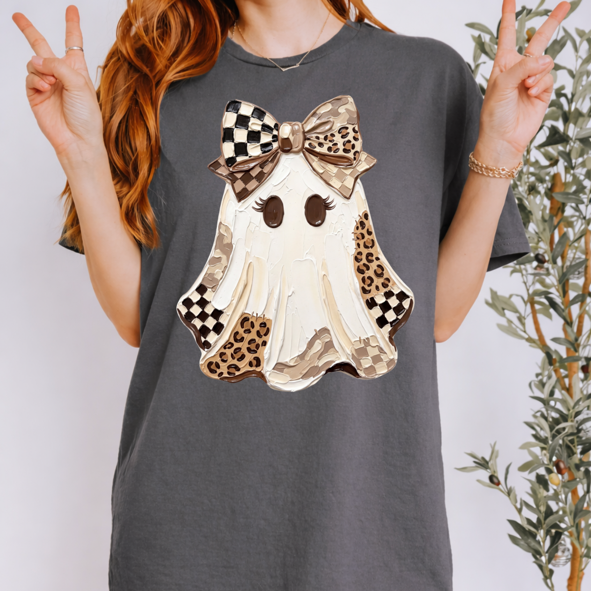 Woman wearing a charcoal Halloween graphic tee with a white ghost, leopard print and checkered details, and a large bow.