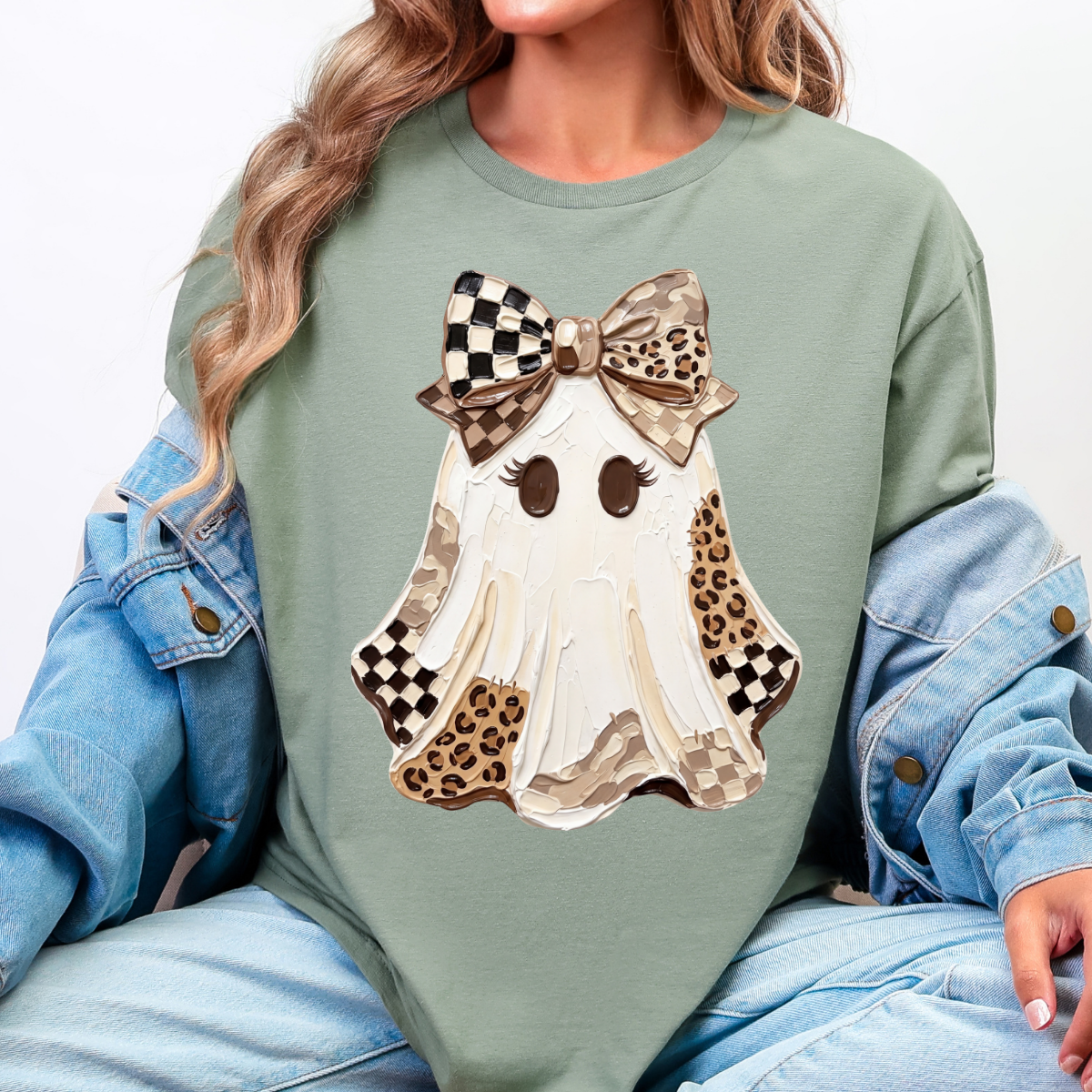 Woman wearing a sage Halloween graphic tee with a white ghost, leopard print and checkered details, and a large bow.