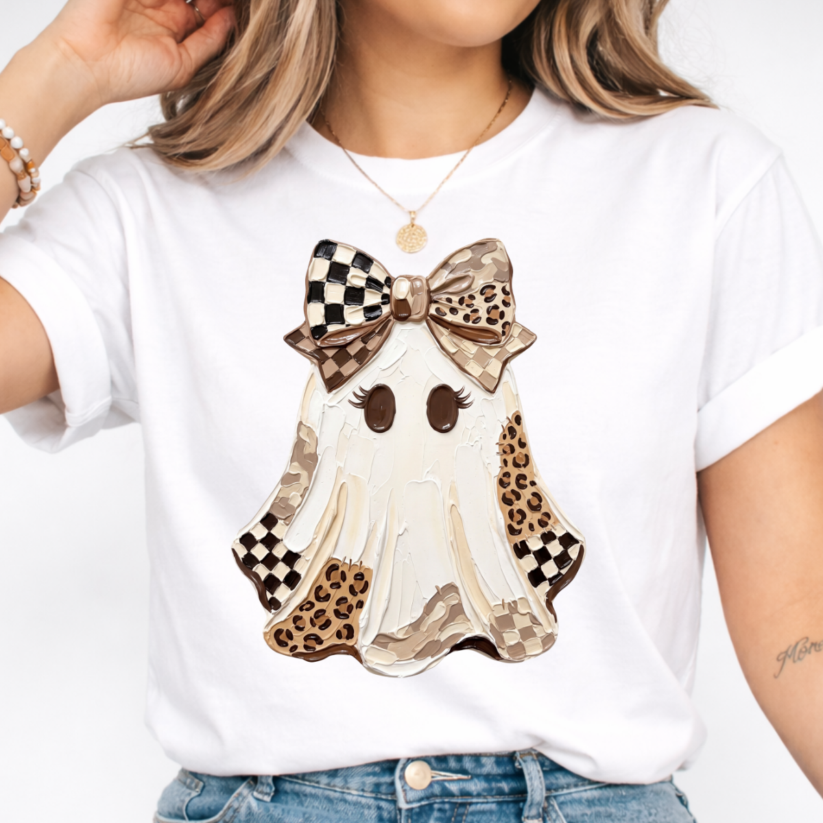 Woman wearing a white Halloween graphic tee with a white ghost, leopard print and checkered details, and a large bow.