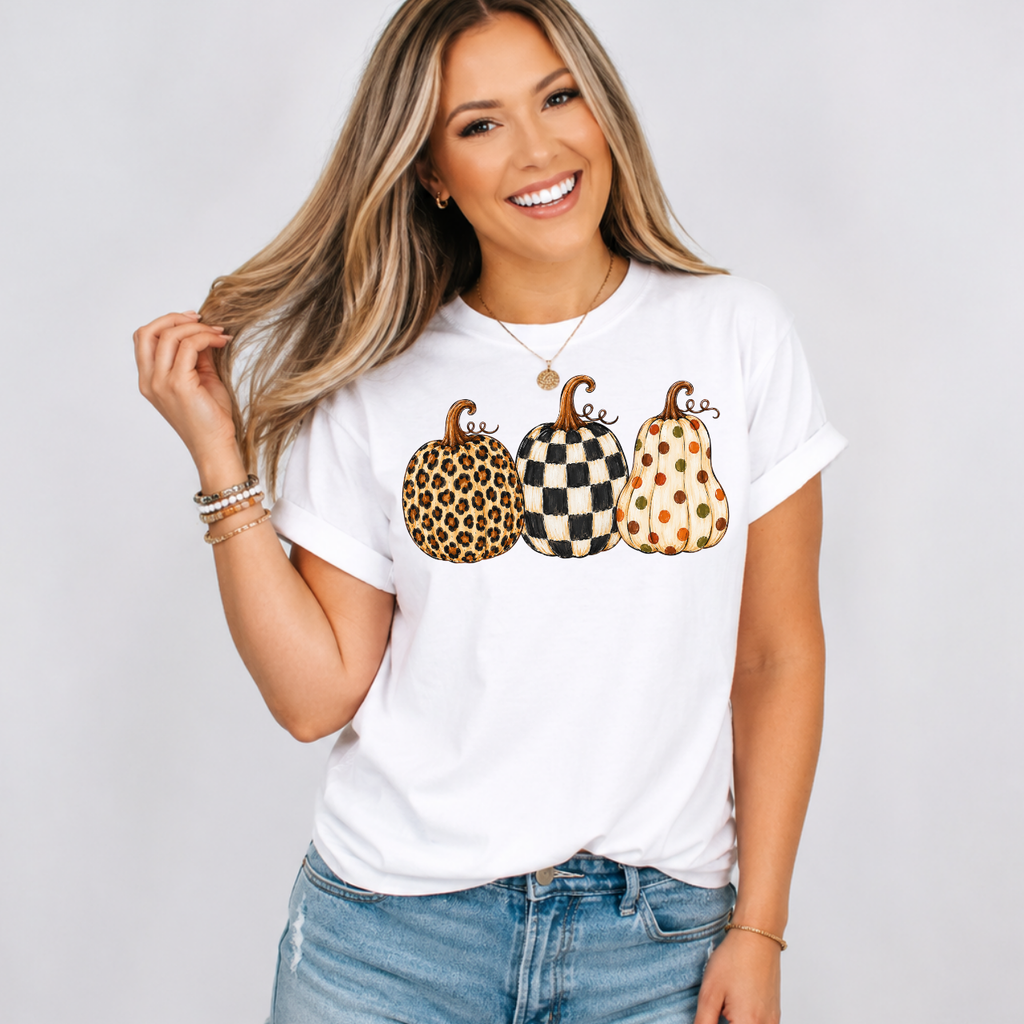Woman wearing a white fall graphic tee with leopard, black-and-white checkered, and polka-dot pumpkins.