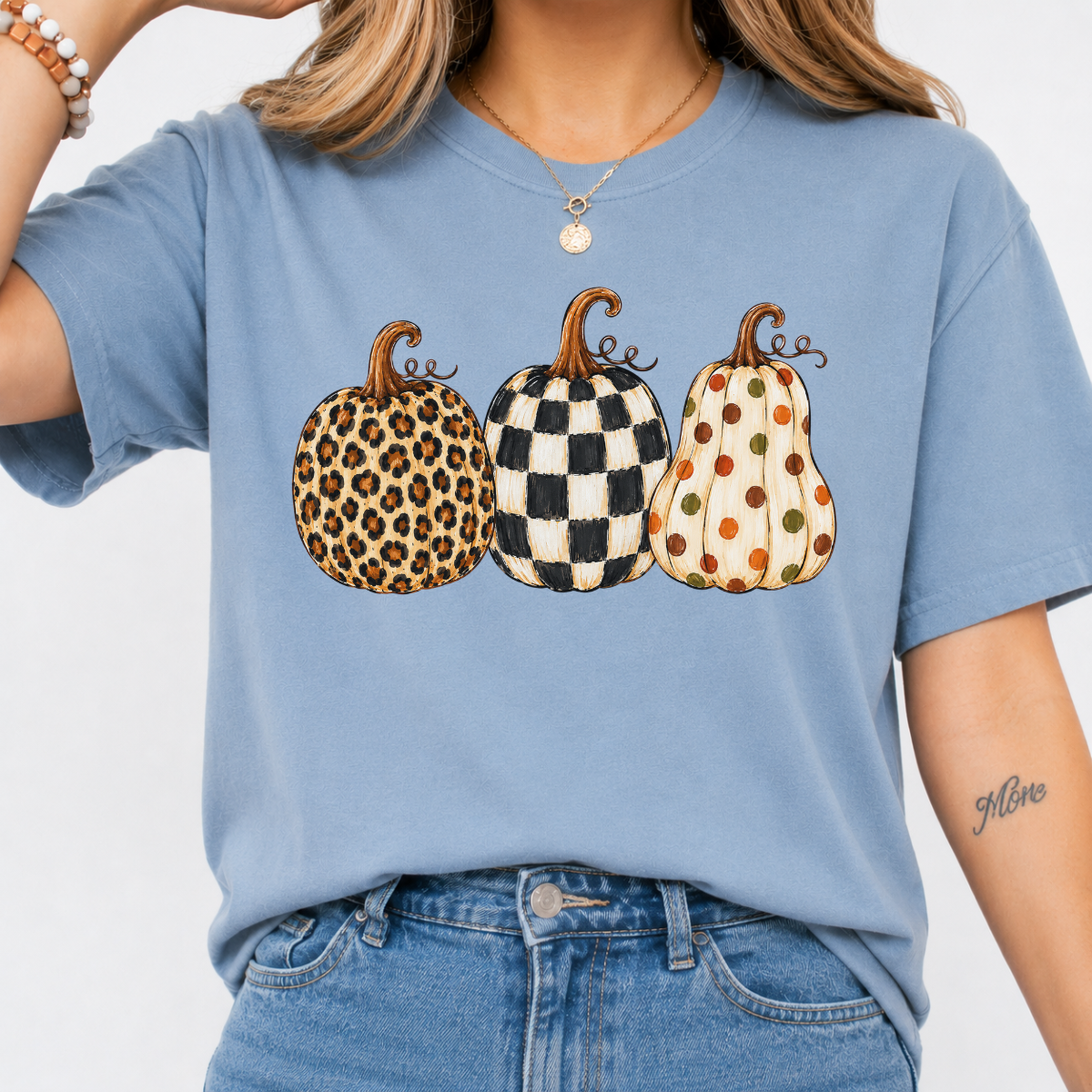 Woman wearing a blue fall graphic tee with leopard, black-and-white checkered, and polka-dot pumpkins