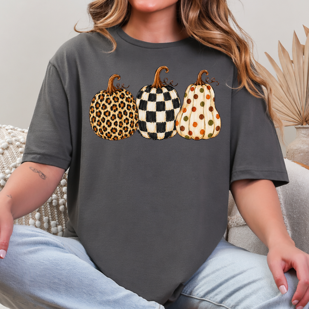 Woman wearing a gray fall graphic tee with leopard, black-and-white checkered, and polka-dot pumpkins