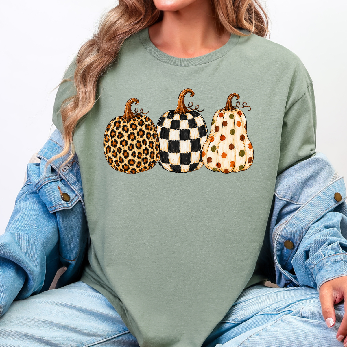 Woman wearing a green fall graphic tee with leopard, black-and-white checkered, and polka-dot pumpkins