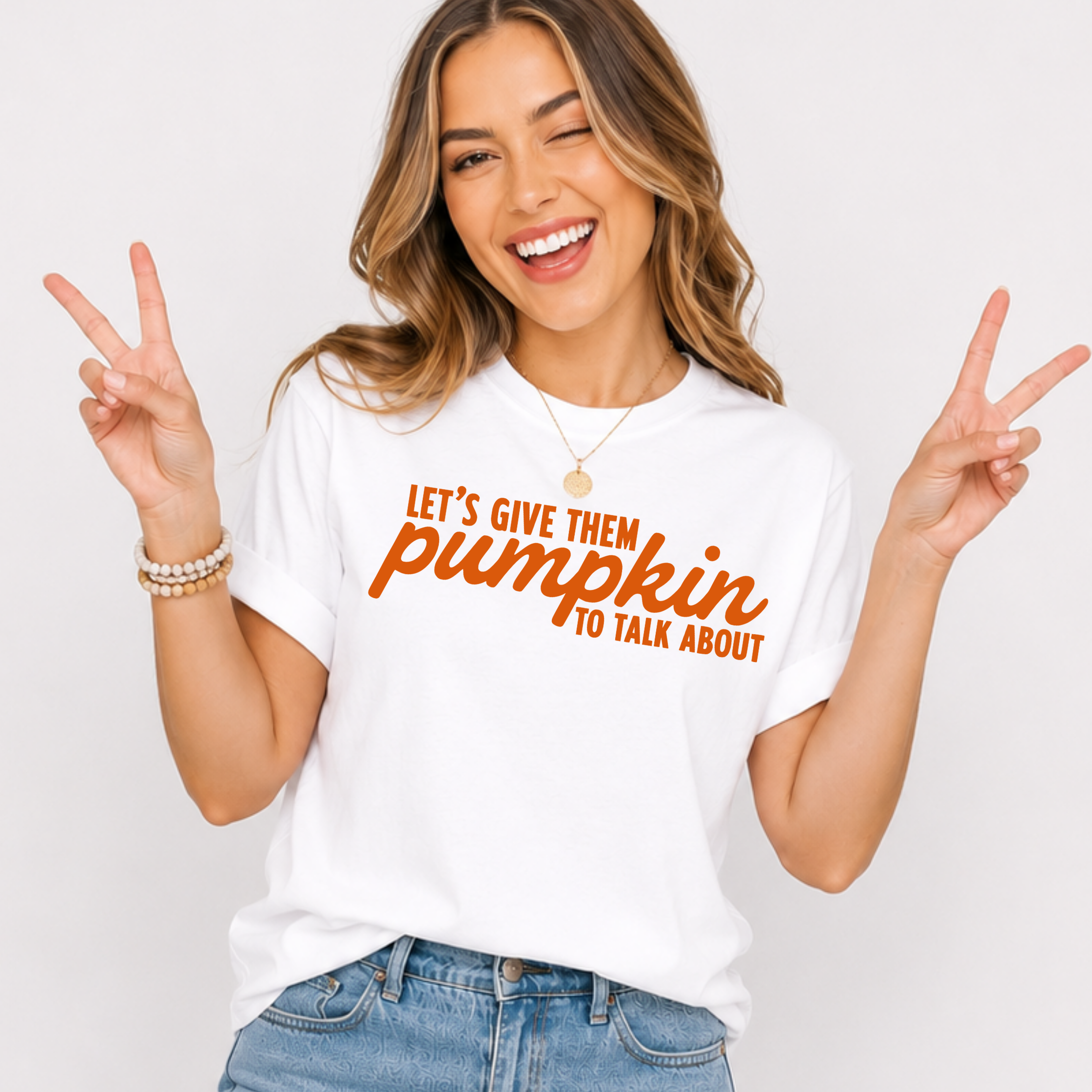Woman wearing a white Let’s Give Them Pumpkin to Talk About fall graphic tee with orange lettering.