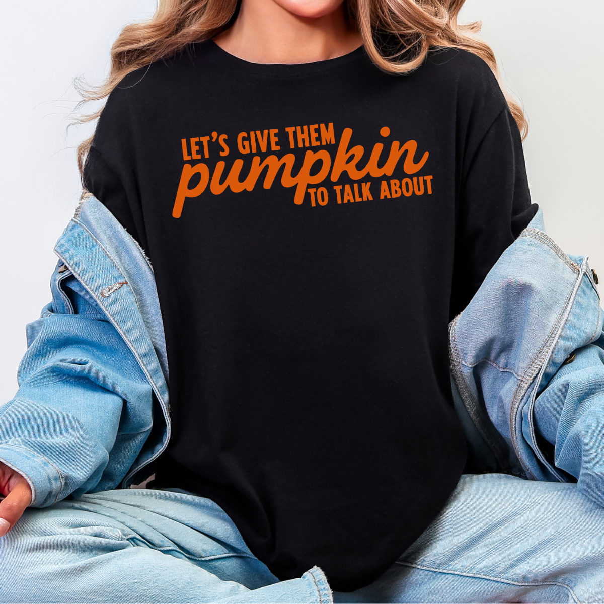 Woman wearing a black Let’s Give Them Pumpkin to Talk About fall graphic tee with orange lettering.