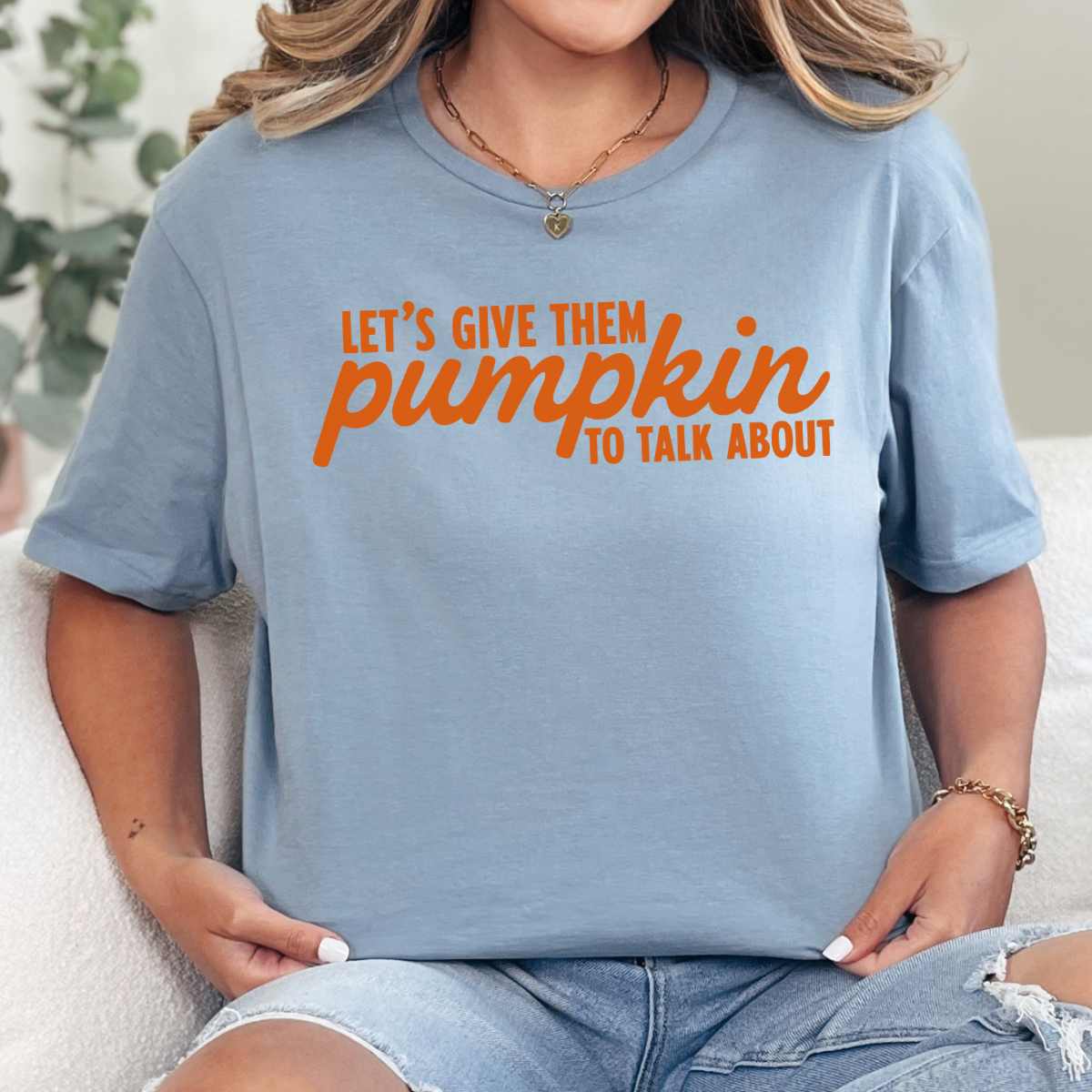Woman wearing a stone blue Let’s Give Them Pumpkin to Talk About fall graphic tee with orange lettering.