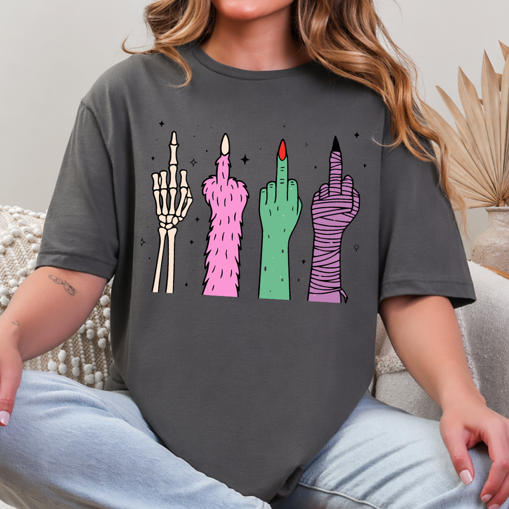 Woman wearing a charcoal Halloween graphic tee with colorful skeleton, monster, witch, and mummy middle finger hands.
