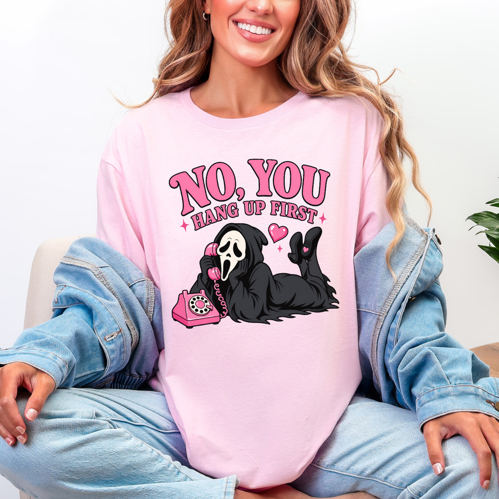 Woman wearing a light pink No You Hang Up First Halloween graphic tee with a masked horror character and pink telephone.
