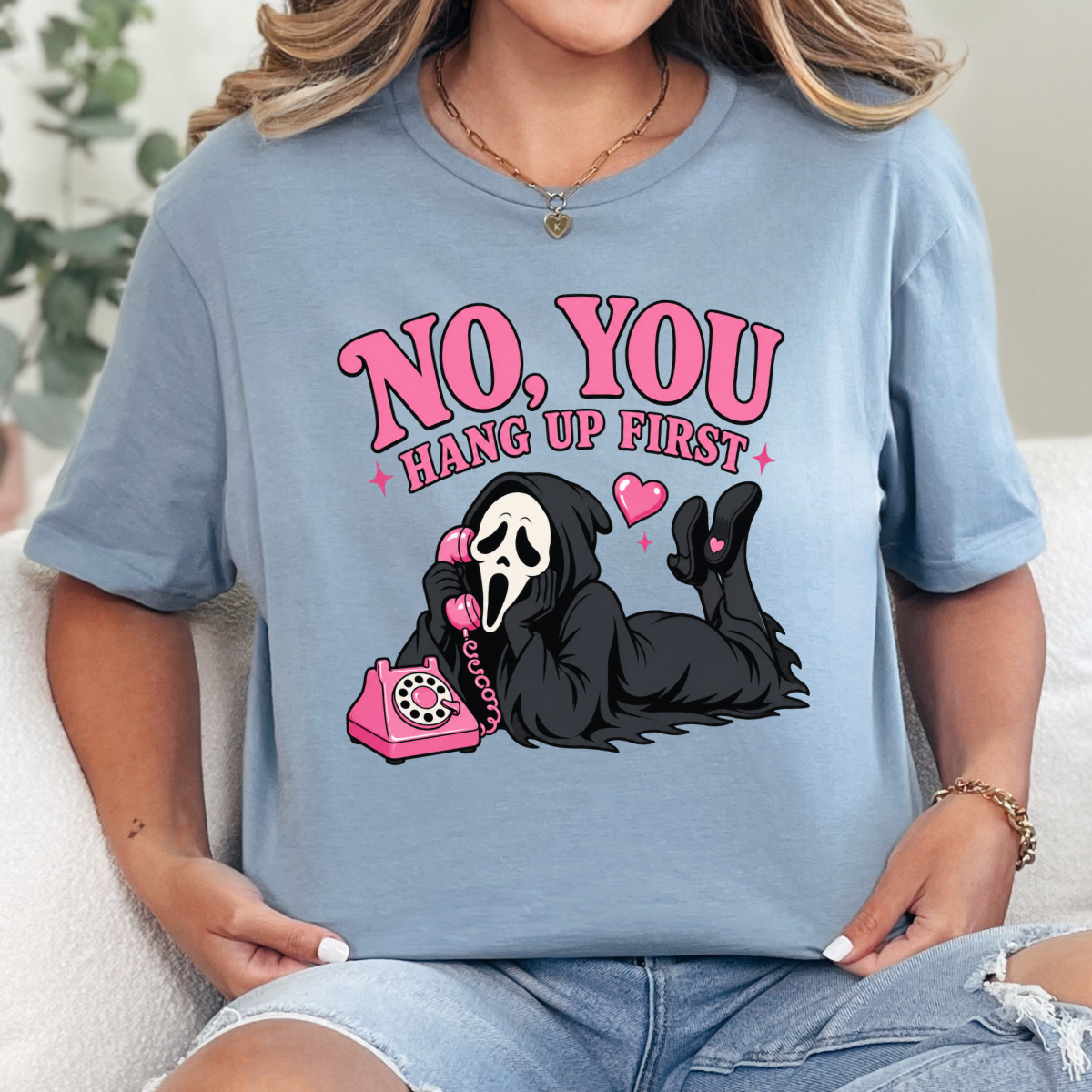 Woman wearing a stone blue No You Hang Up First Halloween graphic tee with a masked horror character and pink telephone.