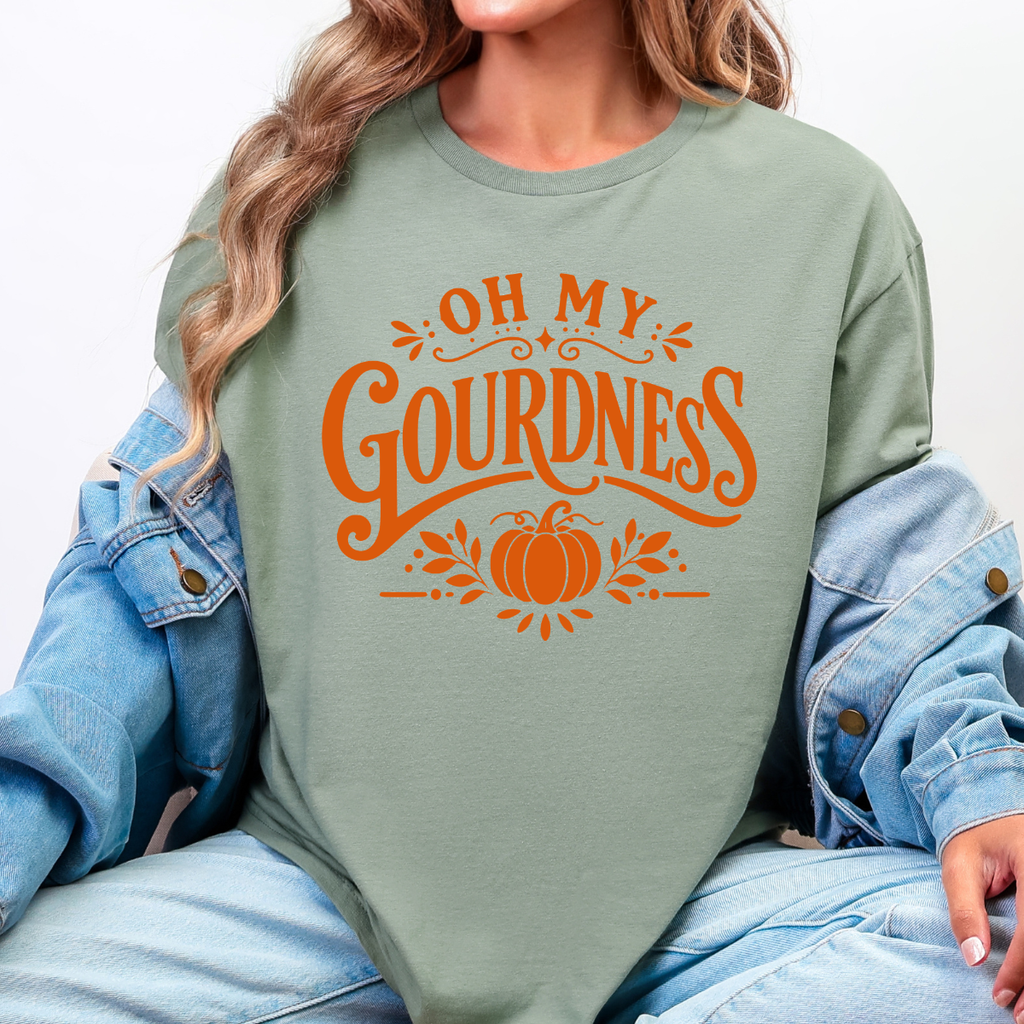 Woman wearing a sage green Oh My Gourdness fall graphic tee with orange lettering and a pumpkin design.