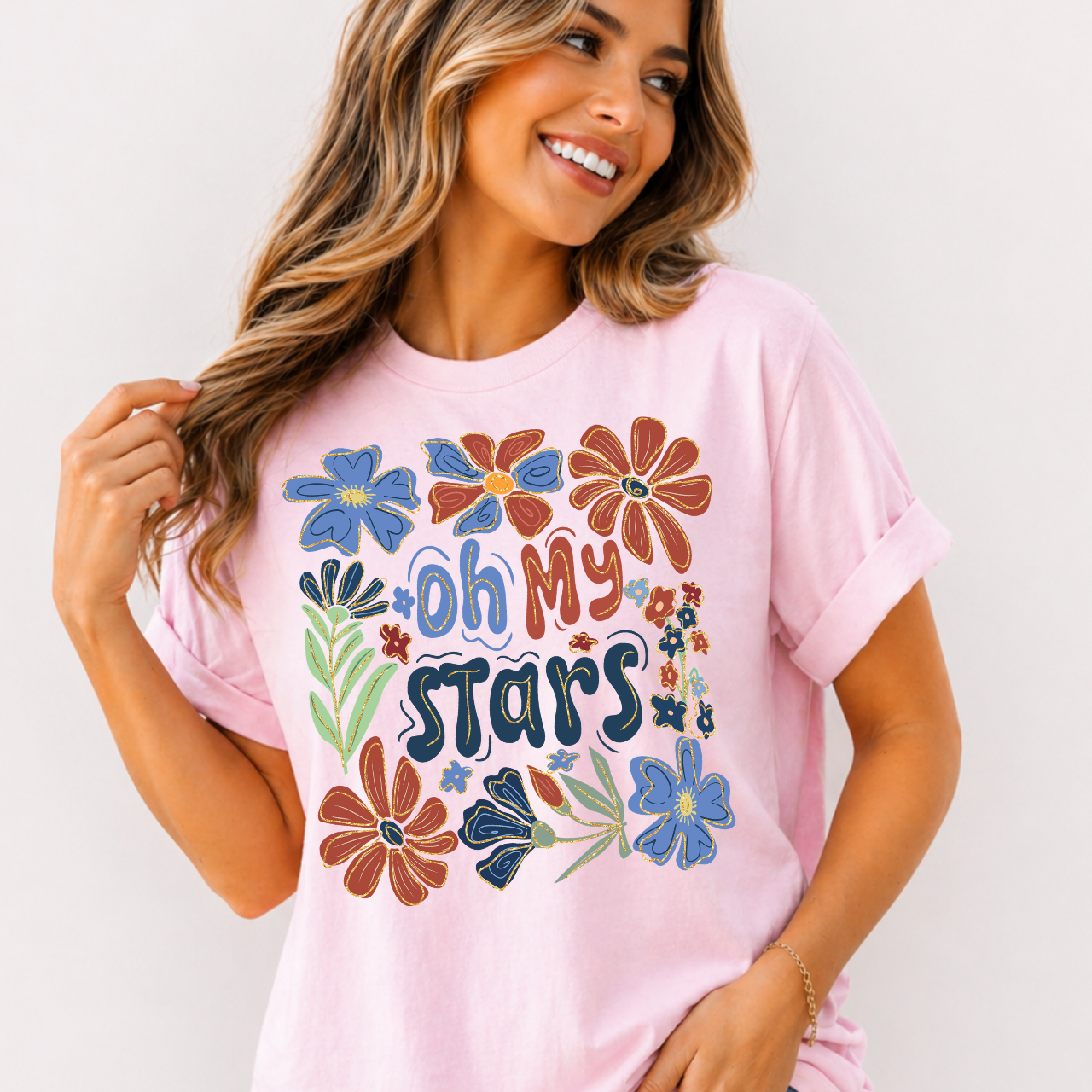 Woman wearing a pink t-shirt with colorful floral designs and 'Oh My Stars' text.