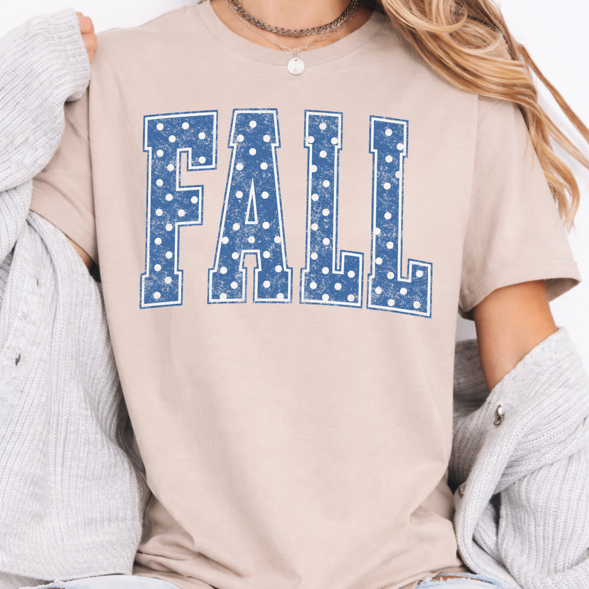 Woman wearing a sand Fall graphic tee with blue polka dot collegiate lettering.