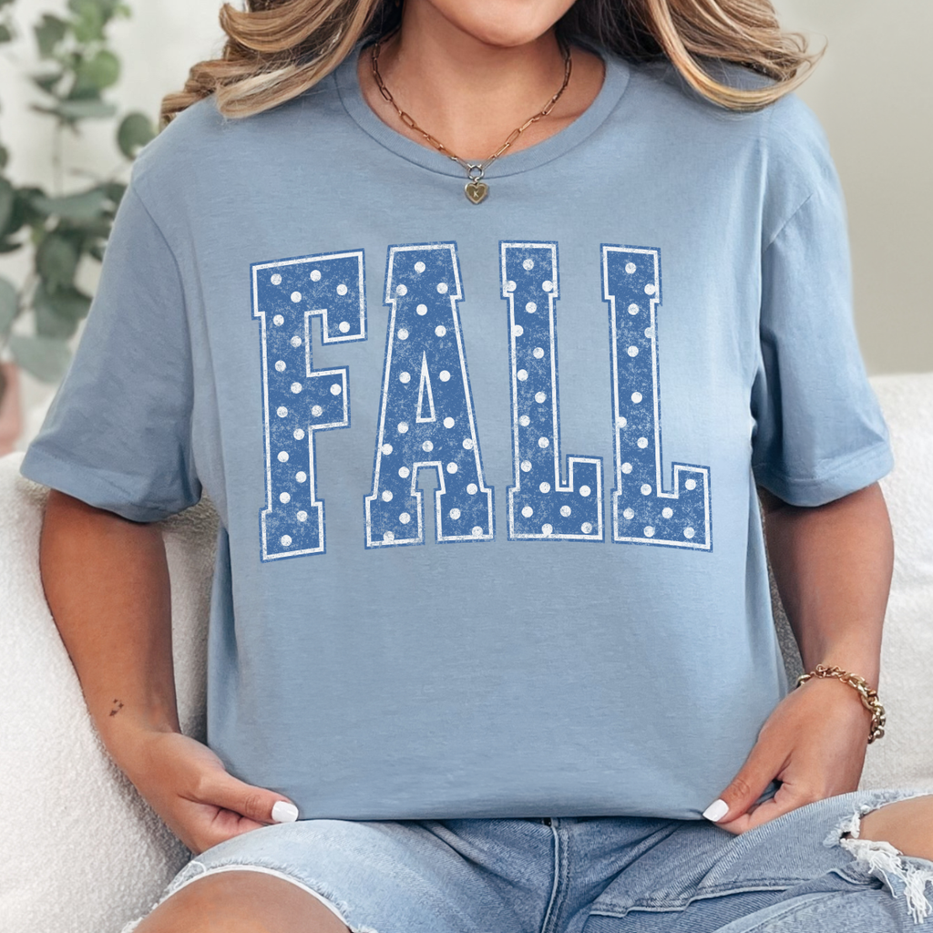 Woman wearing a stone blue Fall graphic tee with blue polka dot collegiate lettering.