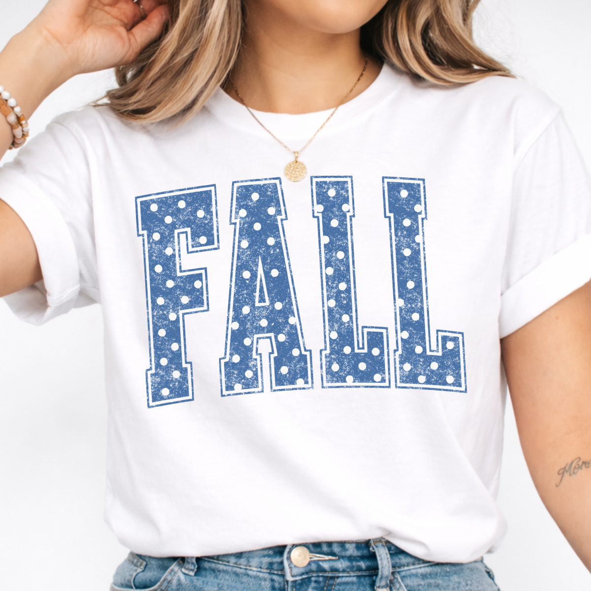 Woman wearing a white Fall graphic tee with blue polka dot collegiate lettering.