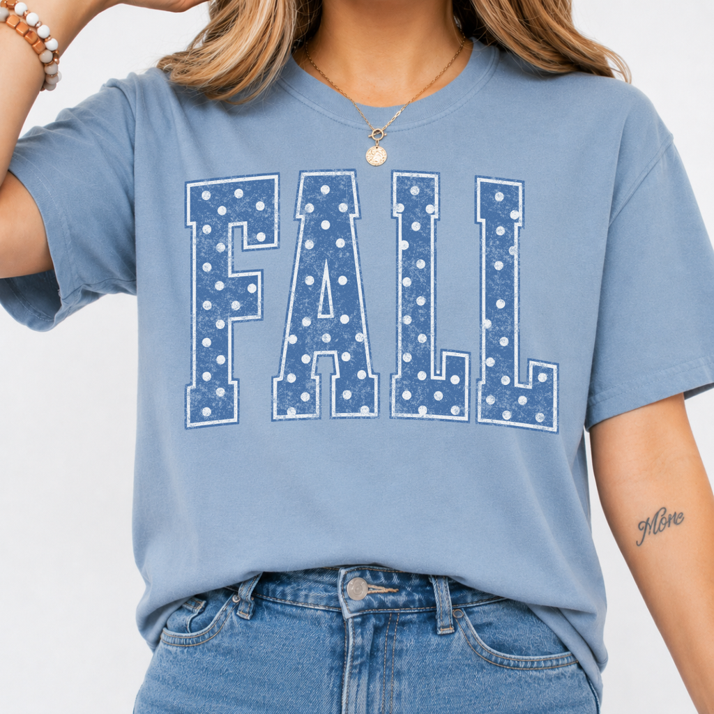 Woman wearing a stone blue Fall graphic tee with blue polka dot collegiate lettering.
