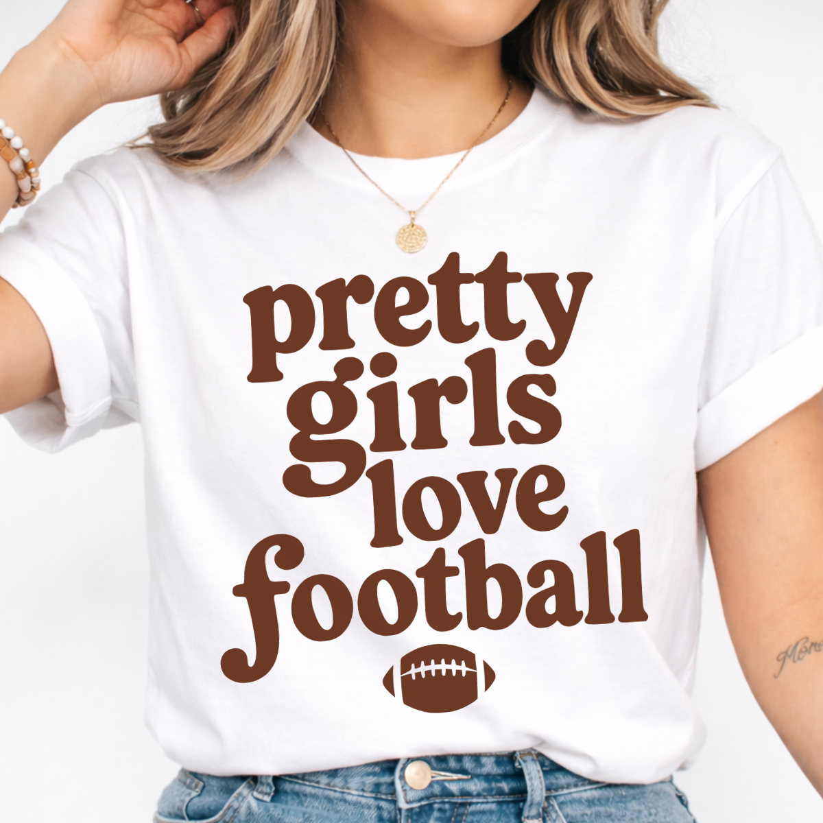 Woman wearing a white Pretty Girls Love Football graphic tee with brown retro lettering and a football design.