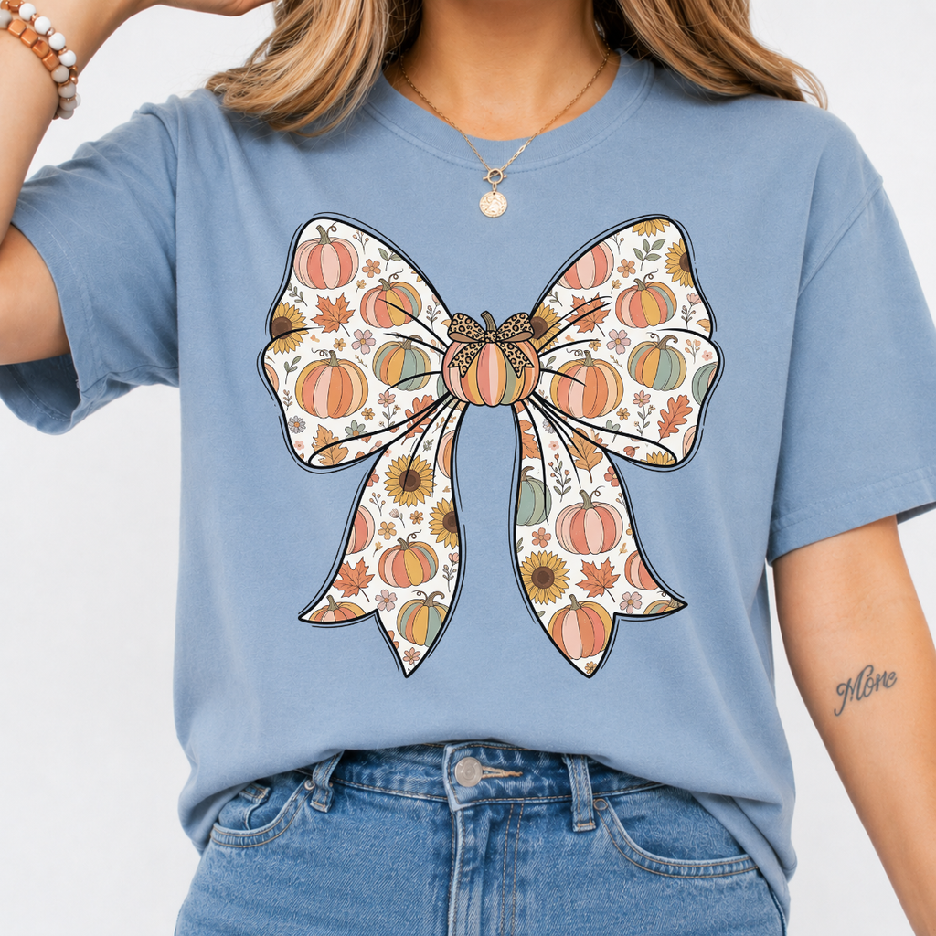 Woman wearing a stone blue fall graphic tee with a large bow filled with pumpkins, sunflowers, and autumn leaves.