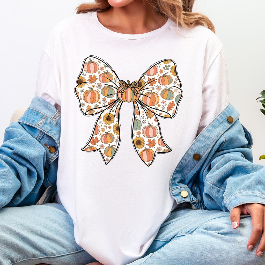 Woman wearing a white fall graphic tee with a large bow filled with pumpkins, sunflowers, and autumn leaves.
