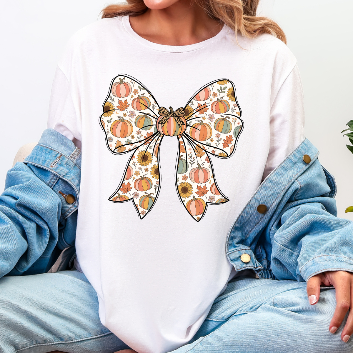 Woman wearing a white fall graphic tee with a large bow filled with pumpkins, sunflowers, and autumn leaves.