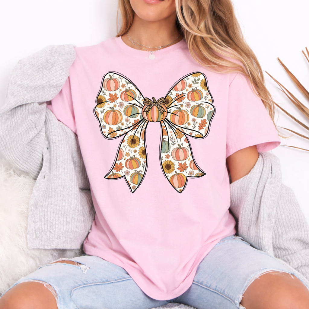 Woman wearing a light pink fall graphic tee with a large bow filled with pumpkins, sunflowers, and autumn leaves.