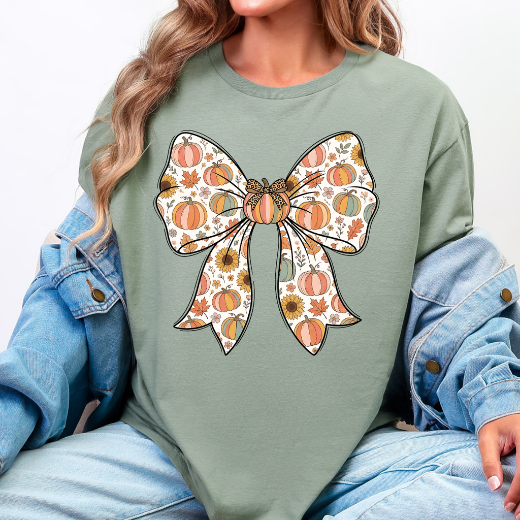 Woman wearing a sage green fall graphic tee with a large bow filled with pumpkins, sunflowers, and autumn leaves.