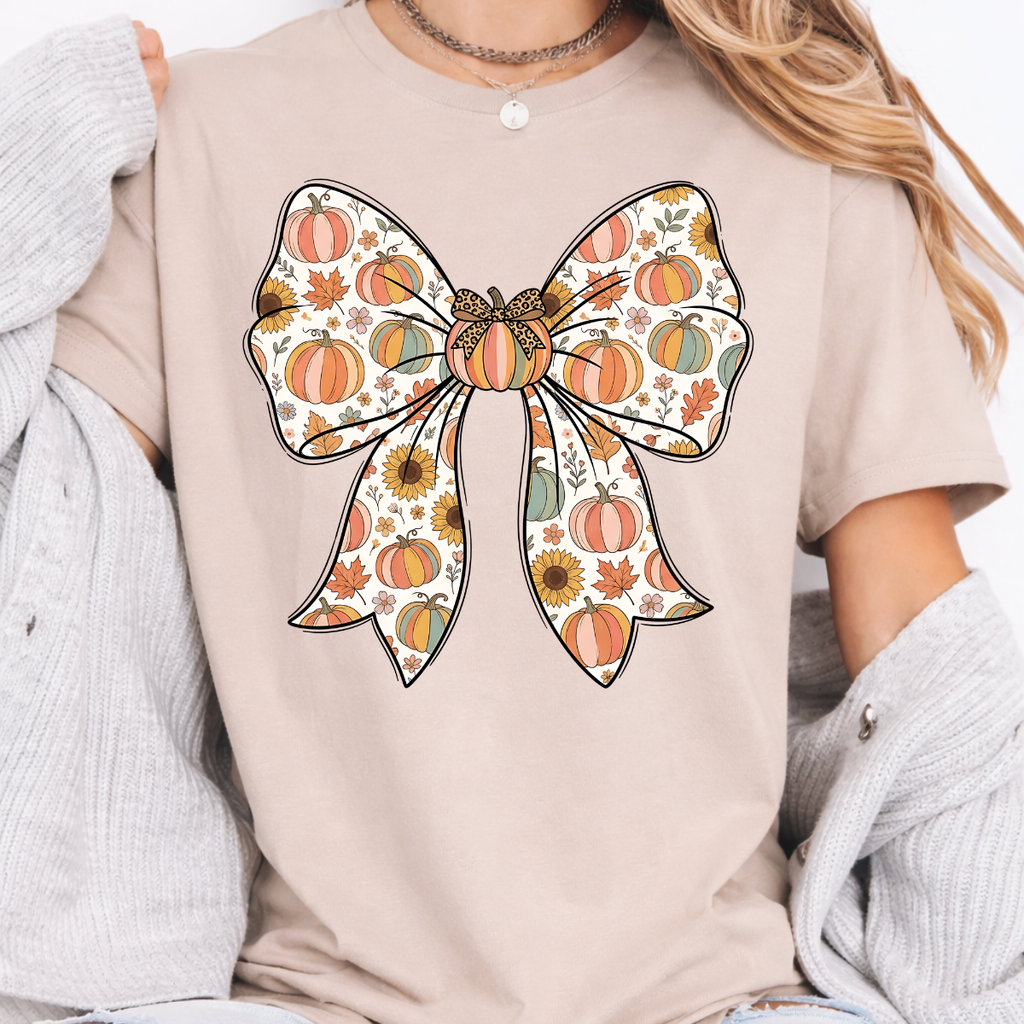 Woman wearing a sand fall graphic tee with a large bow filled with pumpkins, sunflowers, and autumn leaves.