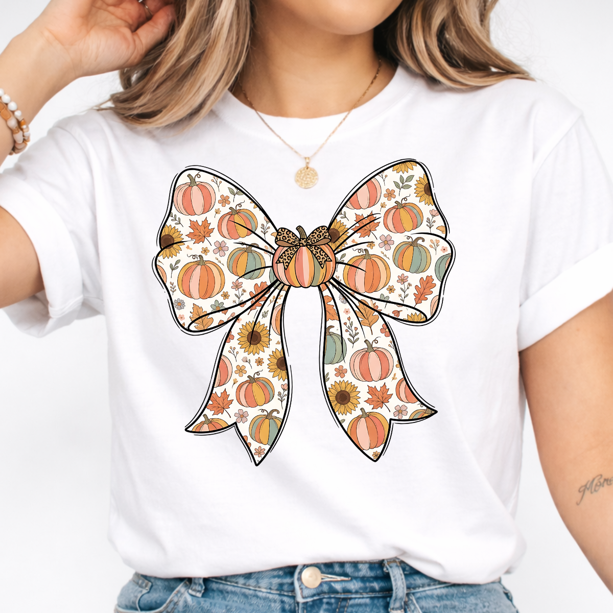 Woman wearing a white fall graphic tee with a large bow filled with pumpkins, sunflowers, and autumn leaves.