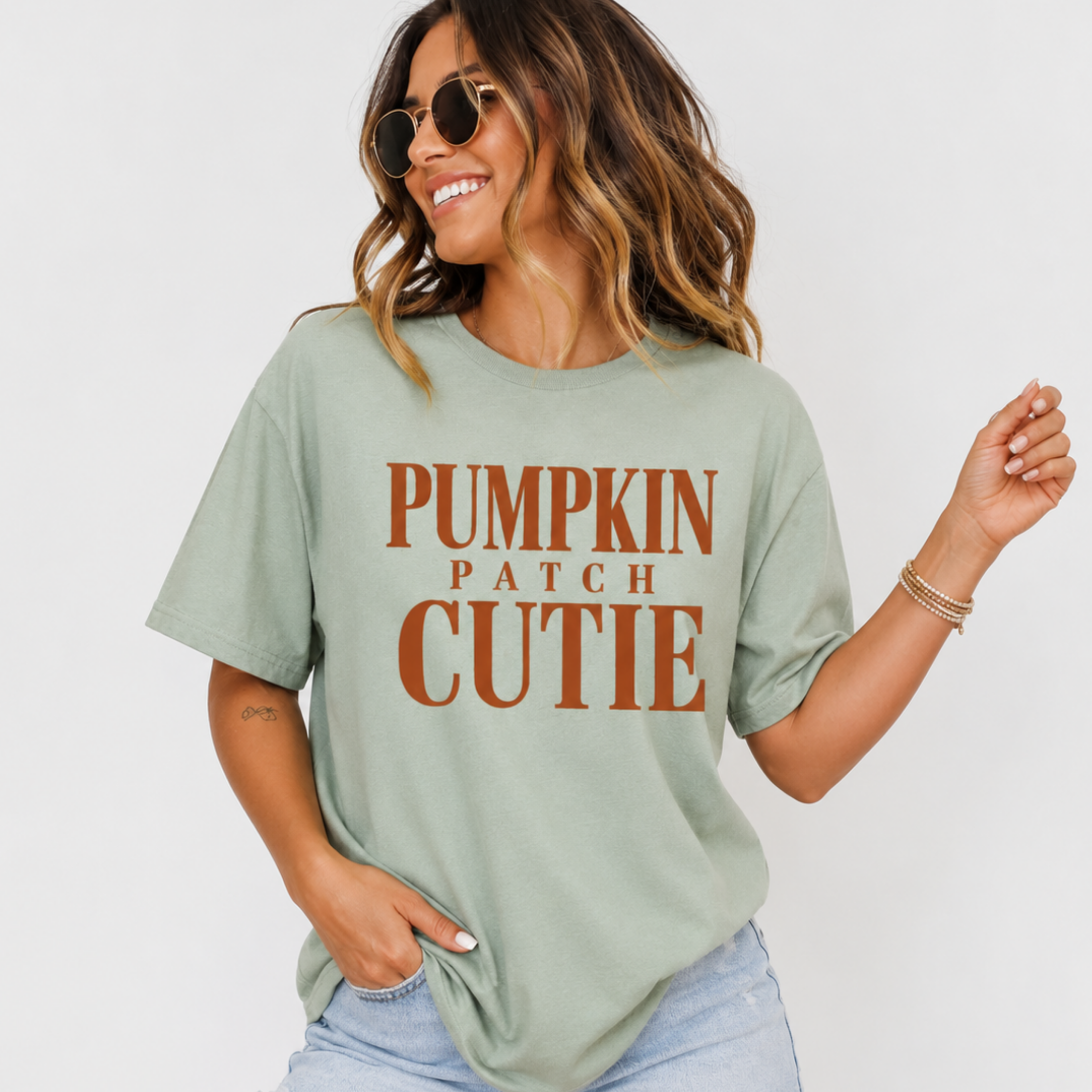 Woman wearing a sage green Pumpkin Patch Cutie fall graphic tee with rust orange lettering.