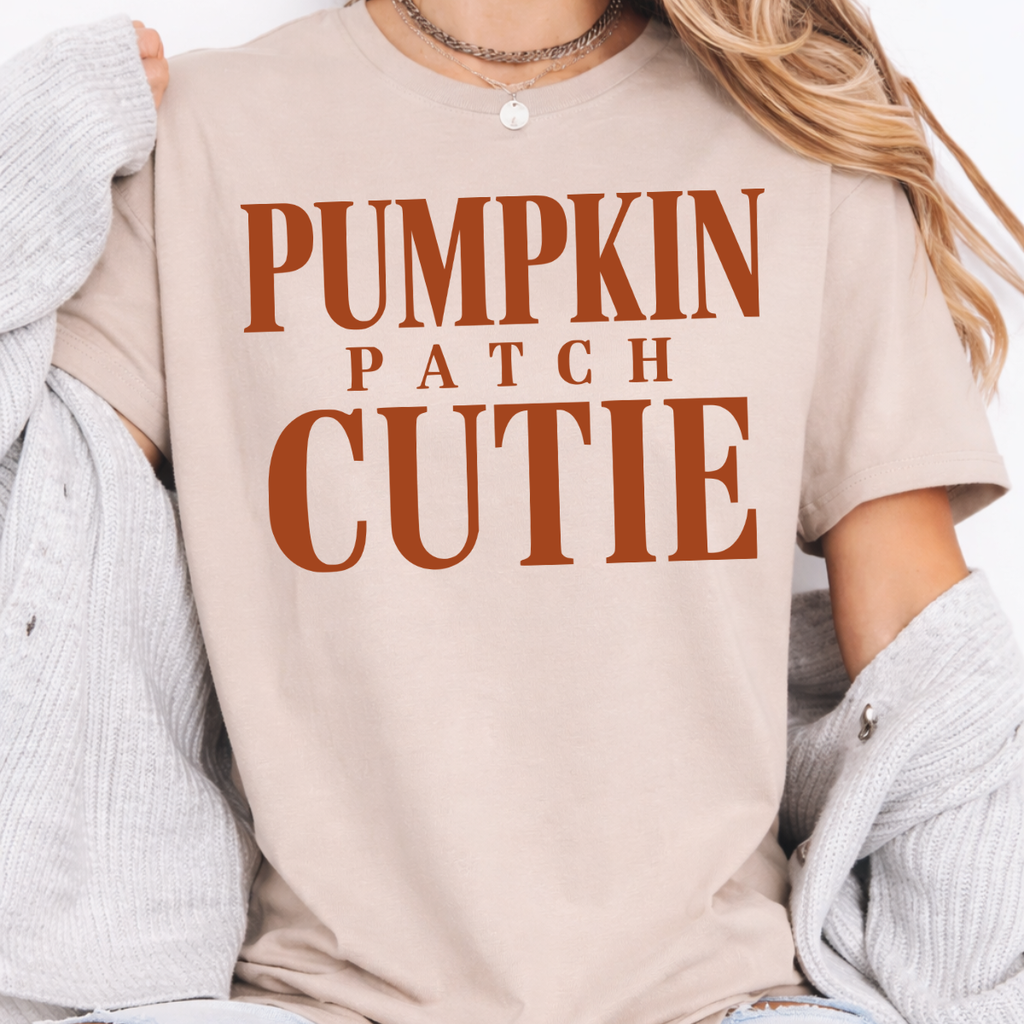 Woman wearing a sand Pumpkin Patch Cutie fall graphic tee with rust orange lettering.