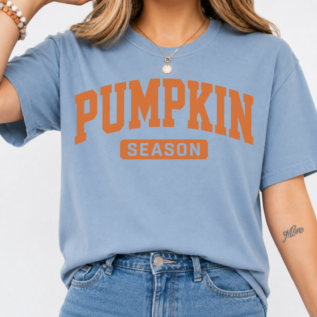 Woman wearing a stone blue Pumpkin Season fall graphic tee with bold orange collegiate lettering.