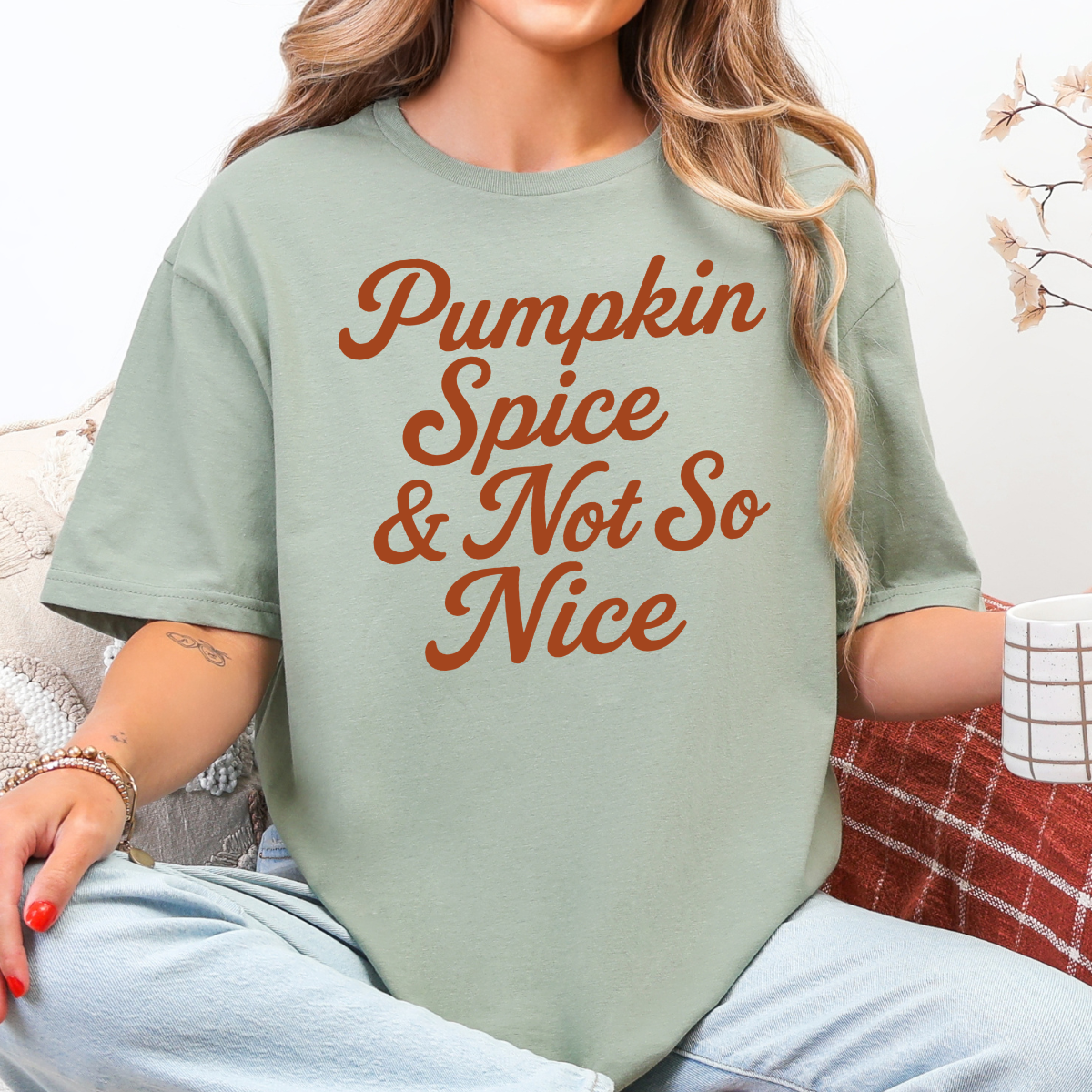 Woman wearing a sage Pumpkin Spice and Not So Nice fall graphic tee with rust orange script lettering.