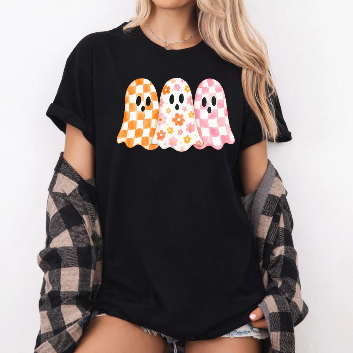Woman wearing a  black Halloween graphic tee with three orange, floral, and pink patterned ghosts.