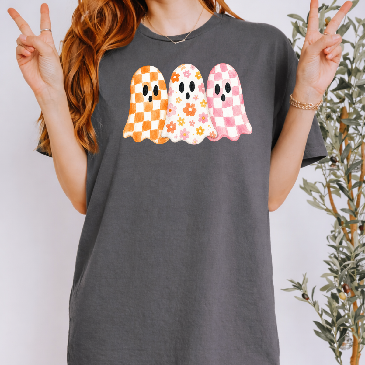 Woman wearing a charcoal Halloween graphic tee with three orange, floral, and pink patterned ghosts.