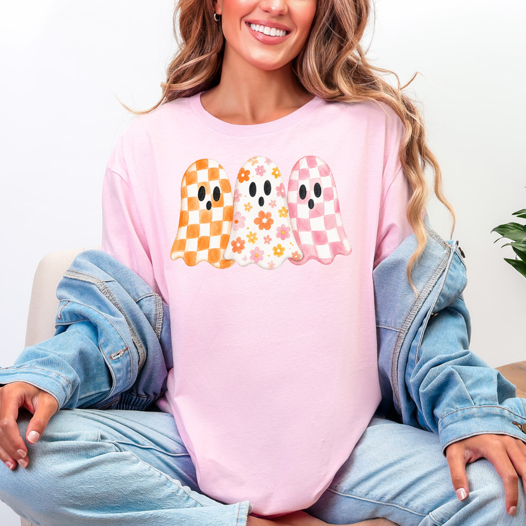 Woman wearing a light pink Halloween graphic tee with three orange, floral, and pink patterned ghosts.