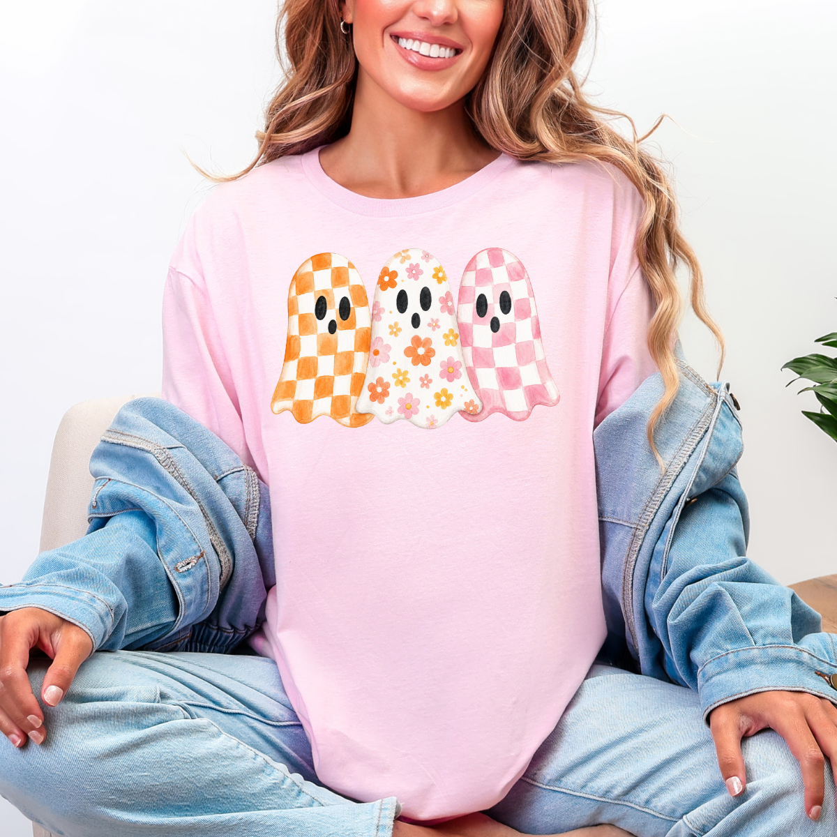 Woman wearing a light pink Halloween graphic tee with three orange, floral, and pink patterned ghosts.