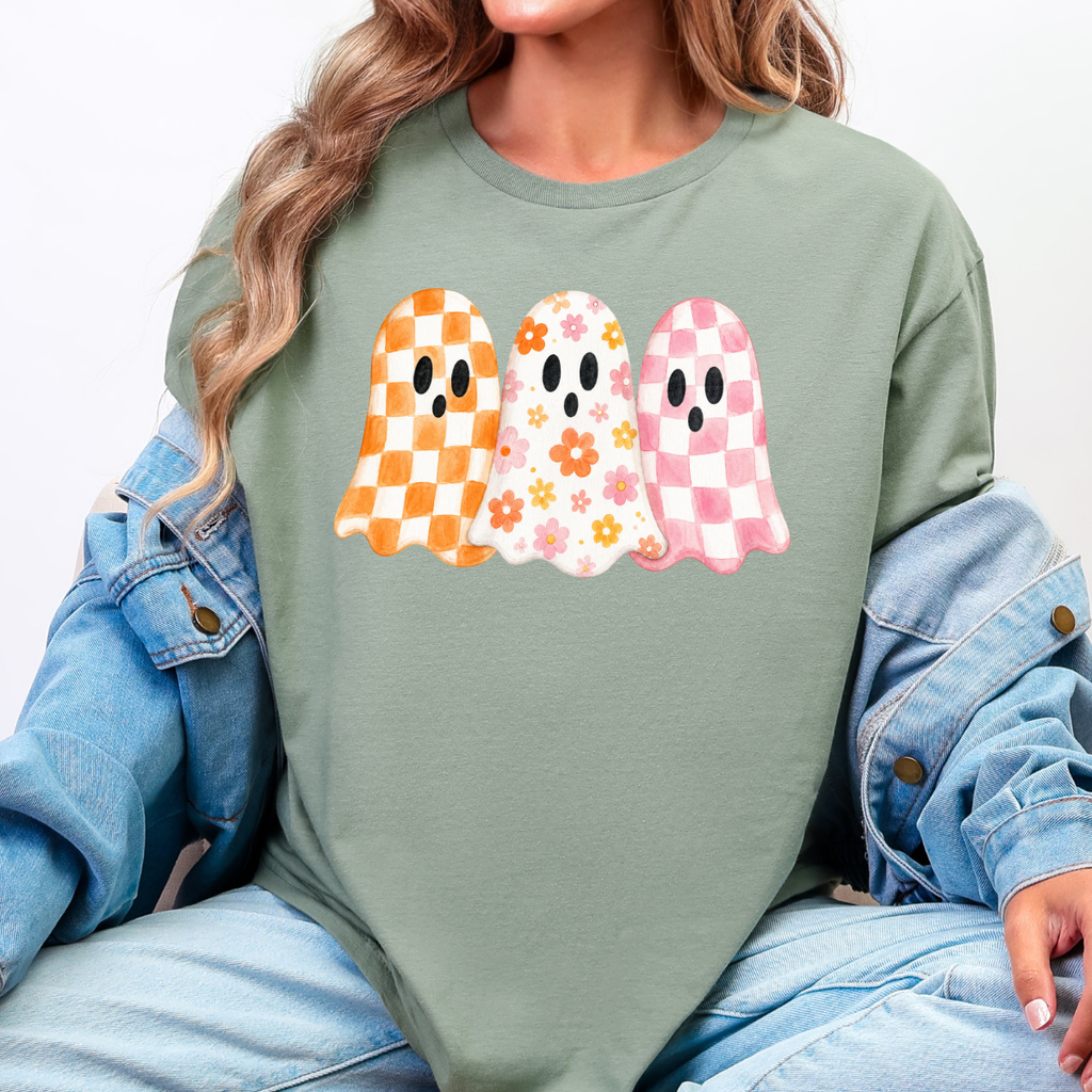 Woman wearing a sage Halloween graphic tee with three orange, floral, and pink patterned ghosts.
