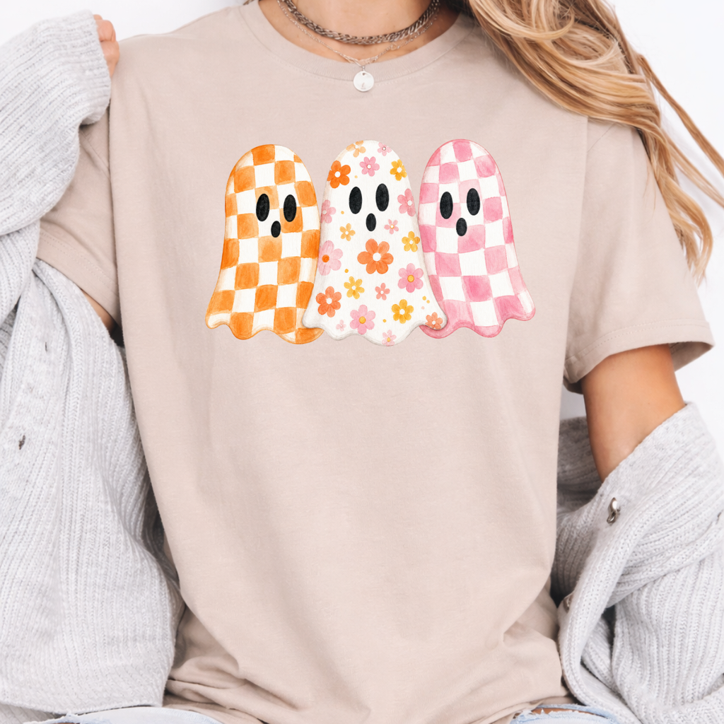 Woman wearing a sand Halloween graphic tee with three orange, floral, and pink patterned ghosts.
