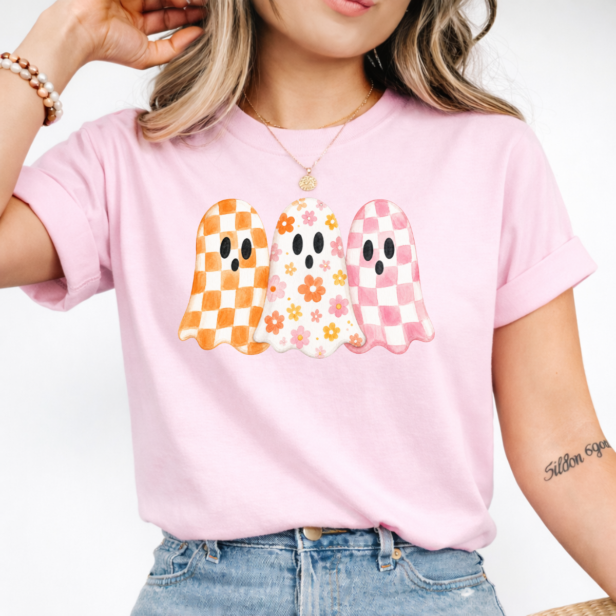 Woman wearing a light pink Halloween graphic tee with three orange, floral, and pink patterned ghosts.