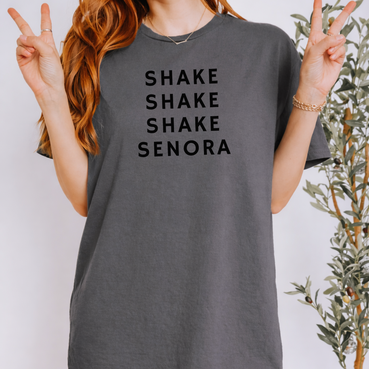 Woman wearing a charcoal Shake Shake Shake Señora Halloween graphic tee with black lettering.