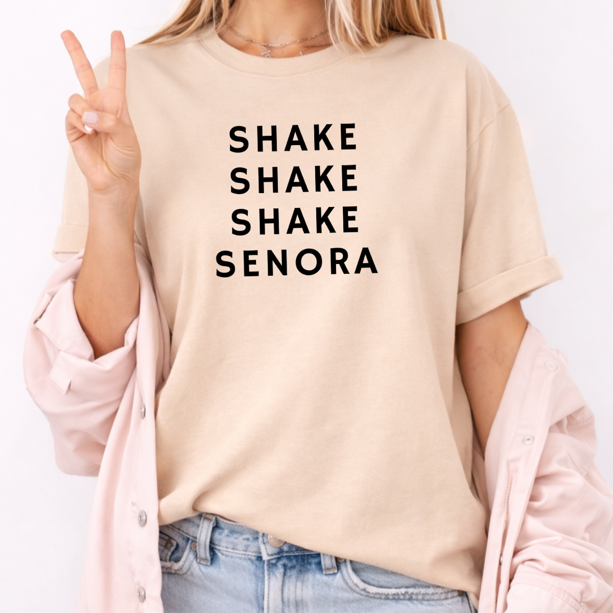 Woman wearing a sand Shake Shake Shake Señora Halloween graphic tee with black lettering.